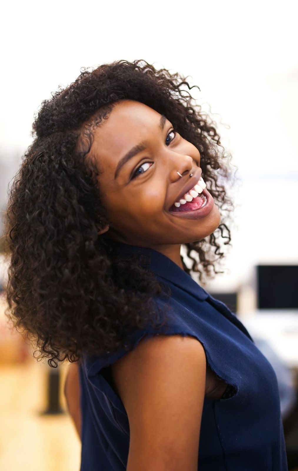 A woman with curly hair laughing as she looks back over her shoulder