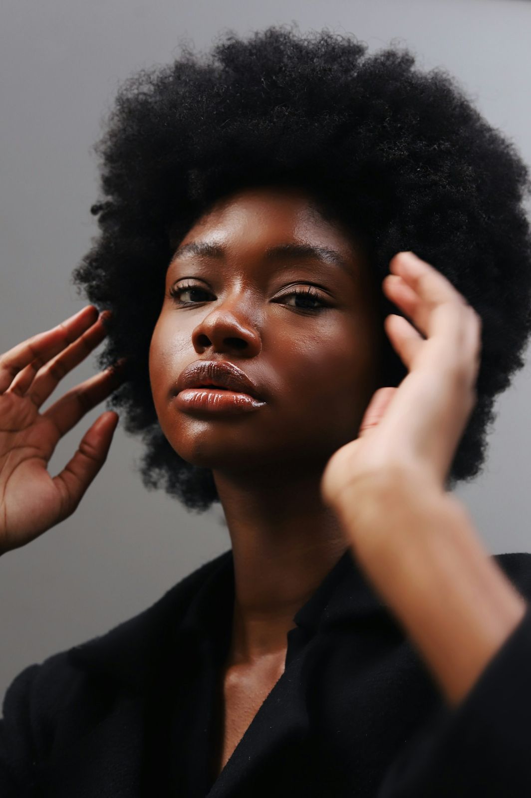 Woman with an afro and glossy lips, hands raised to her hair